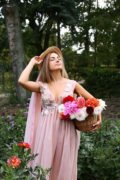 Foto een schattig en stijlvol meisje in een lange jurk en hoed met een mand met bloemen