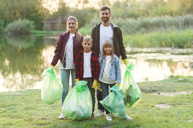 Een schattig gezin van ouders en kinderen houdt plastic vuilniszakken vast na het opruimen van het omliggende gebied bij het meer