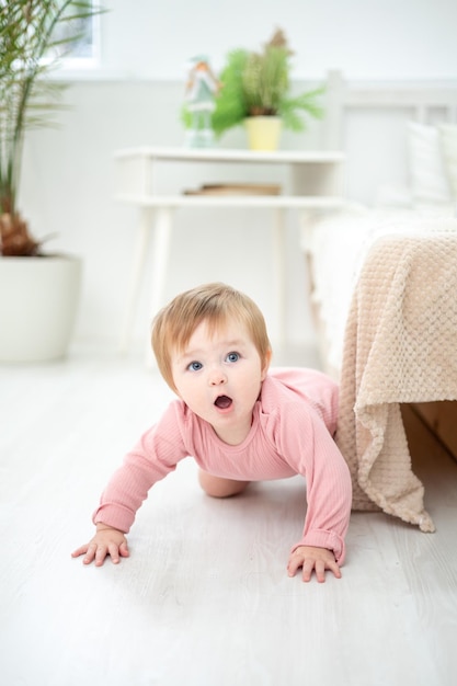 Een schattig gezond meisje staat thuis bij het bed in de slaapkamer de eerste stapjes van de baby de baby leert lopen