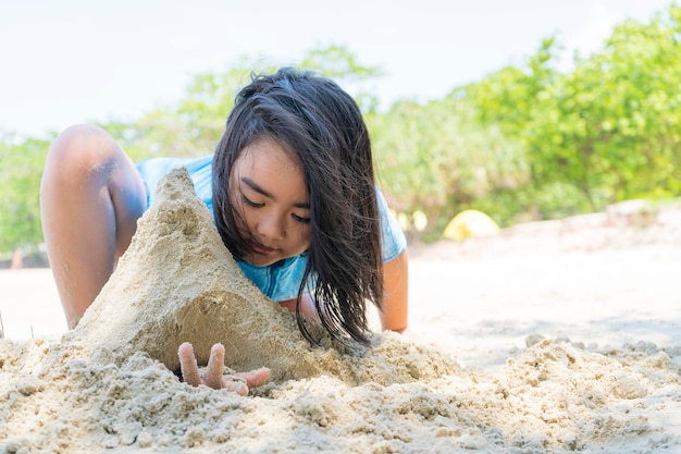 Een schattig jong aziatisch meisje dat alleen op een zandstrand zit en speelt