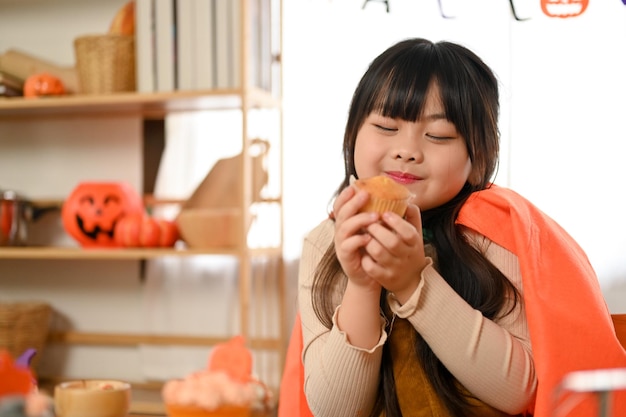 Een schattig jong Aziatisch meisje in Halloween-kostuum met een lekkere Halloween-cupcake