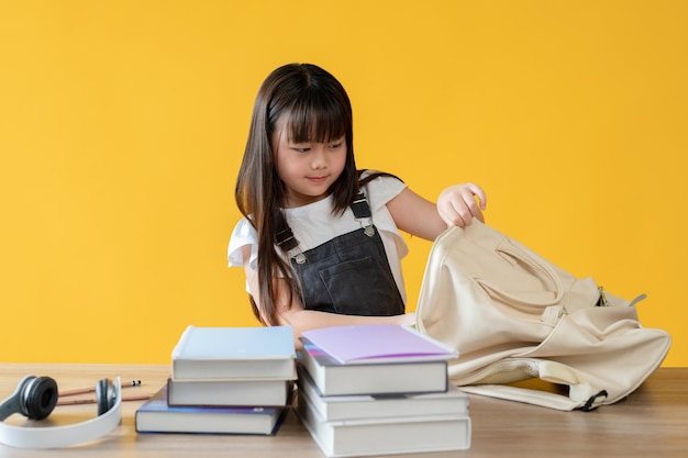 Een schattig jong Aziatisch meisje pakt haar schooltas in en stopt haar boeken in een rugzak