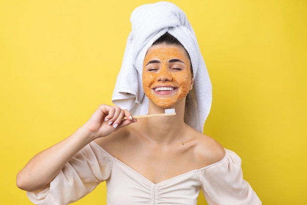 Een schattig jong meisje met een scrubmasker op haar gezicht poetst haar tanden tegen een gele achtergrond