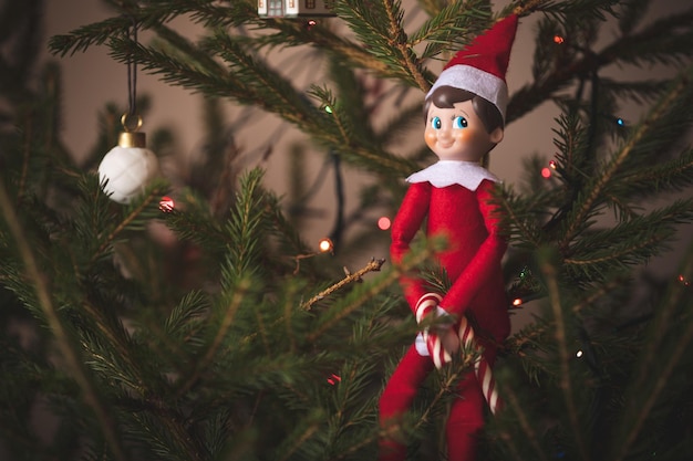 Een schattig kerstspeelgoed zit op een groenblijvende dennenboom versierd met slingers en ander nieuwjaarsspeelgoed