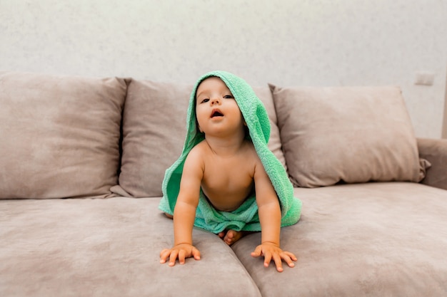 Een schattig kind gewikkeld in een handdoek zit op het bed. baby in een badhanddoek.