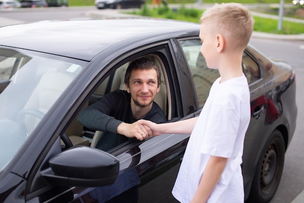 Een schattig kind schudt de hand van een gelukkige vader Papa zit in de auto en lacht