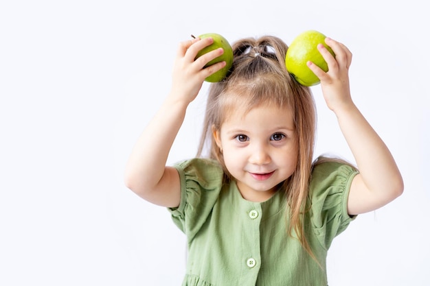 Een schattig klein babymeisje houdt een grote groene appel in haar handen Witte geïsoleerde achtergrond Gezonde voeding voor kinderen of een gezonde snack Ruimte voor tekst Hoogwaardige fotografie