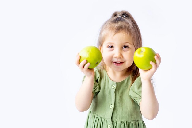 Een schattig klein babymeisje houdt een grote groene appel in haar handen Witte geïsoleerde achtergrond Gezonde voeding voor kinderen of een gezonde snack Ruimte voor tekst Hoogwaardige fotografie