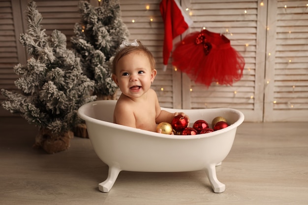 een schattig klein meisje baadt in een badkuip met rood en goud kerstboomspeelgoed het meisje is blij