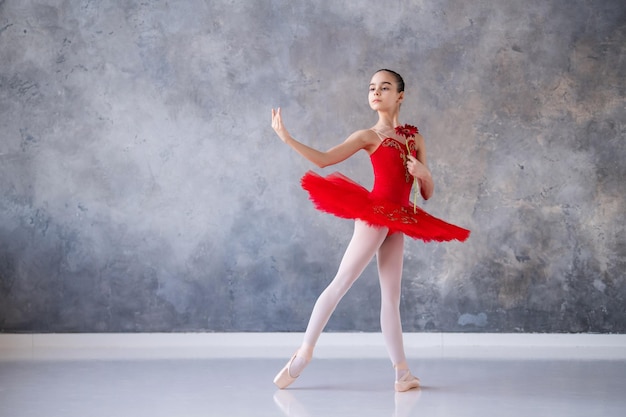Een schattig klein meisje droomt ervan een professionele ballerina te worden Een meisje in een felrode tutu op pointe-schoenen danst in de hal Beroepsschoolstudent