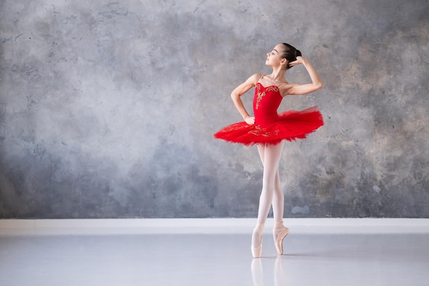 Een schattig klein meisje droomt ervan een professionele ballerina te worden Een meisje in een felrode tutu op pointe-schoenen danst in de hal Beroepsschoolstudent