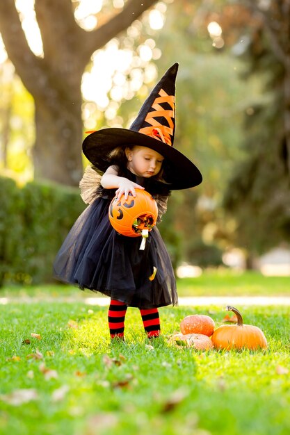 Een schattig klein meisje in een heksenkostuum loopt op straat met een snoepje in de vorm van een pompoen.