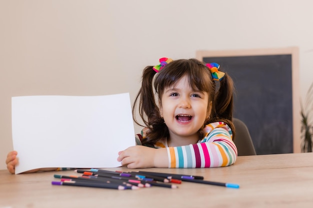 Een schattig klein meisje in een tekenles houdt een leeg wit vel in haar handen een ruimte voor tekst kinderen en creativiteit