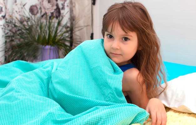 Foto een schattig klein meisje lacht terwijl ze in bed ligt onder een blauwe wollen deken. goede morgen.