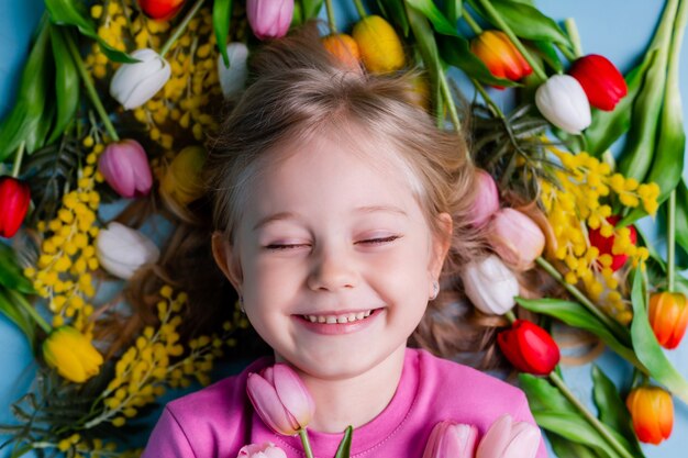 Een schattig klein meisje ligt tussen de tulpen op een blauwe achtergrond in de studio.