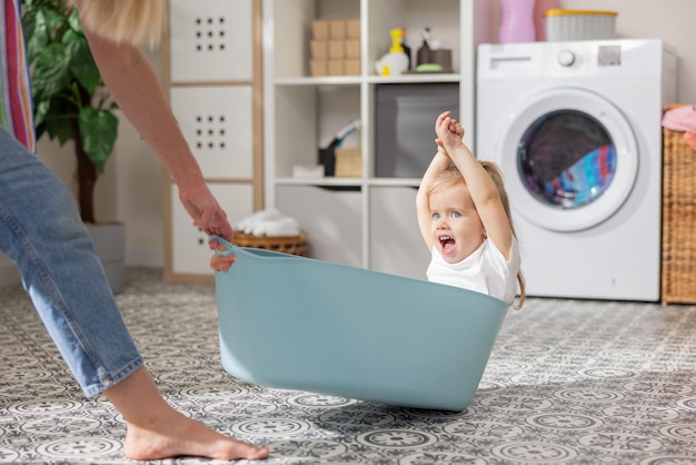 Een schattig klein meisje met blond haar en blauwe ogen zit in een plastic blauwe kledingkom