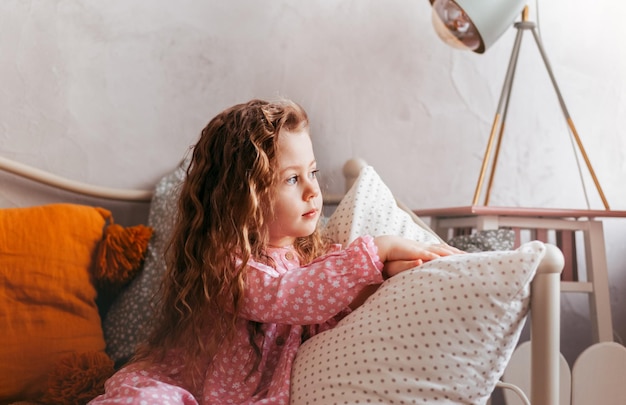 Een schattig klein meisje rust op een bed in een kinderkamer en kijkt uit het raam