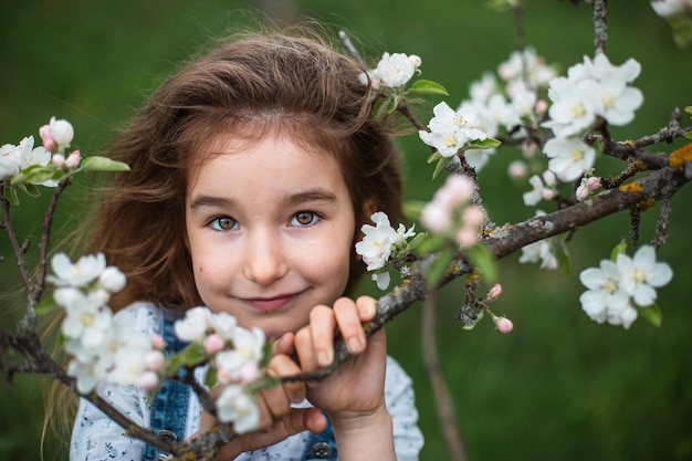 Een schattig klein meisje van 5 jaar oud in een bloeiende witte appelboomgaard in het voorjaar. Lente, boomgaard, bloei, allergie, lentegeur, tederheid, zorg voor de natuur. Portret