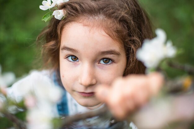 Een schattig klein meisje van 5 jaar oud in een bloeiende witte appelboomgaard in het voorjaar. Lente, boomgaard, bloei, allergie, lentegeur, tederheid, zorg voor de natuur. Portret