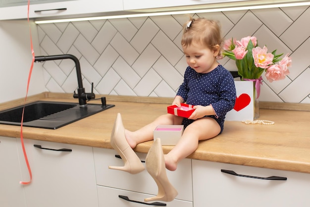 Een schattig klein meisje zit in de keuken met een boeket roze tulpen mooie cadeau ansichtkaart