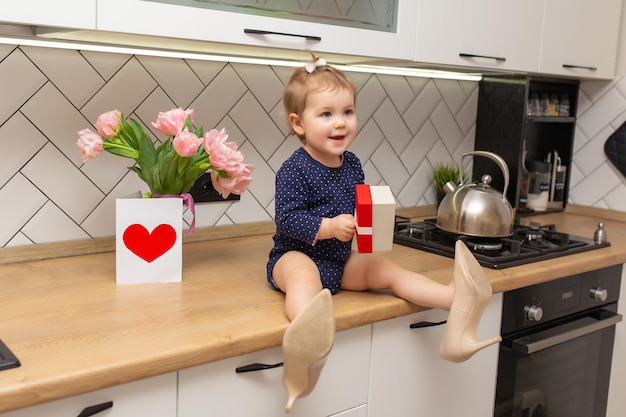 Een schattig klein meisje zit in de keuken met een boeket roze tulpen mooie cadeau ansichtkaart