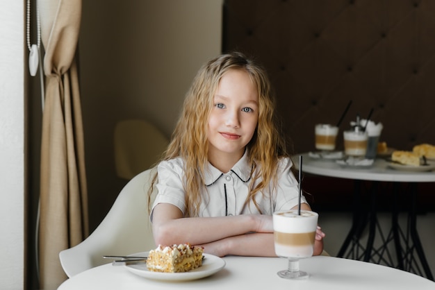 Een schattig klein meisje zit in een cafe en kijkt naar een cake en cacao close-up. dieet en goede voeding.