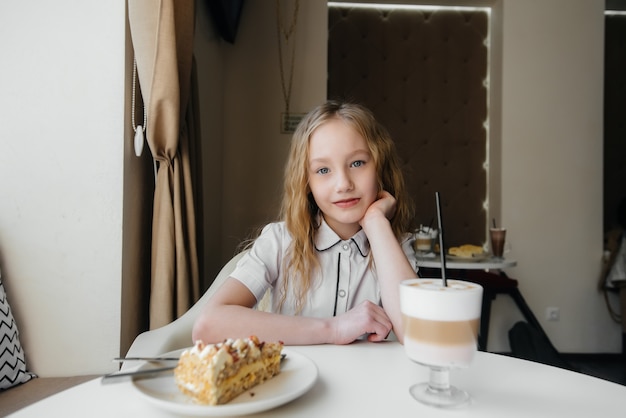 Een schattig klein meisje zit in een cafe en kijkt naar een cake en cacao close-up. Dieet en goede voeding.