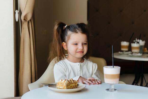 Een schattig klein meisje zit in een cafe en kijkt naar een cake en cacao close-up.