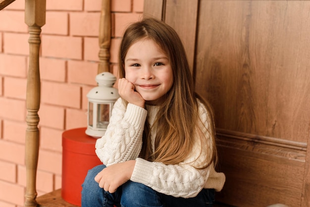 Foto een schattig klein meisje zit op de veranda van de kerstdeur