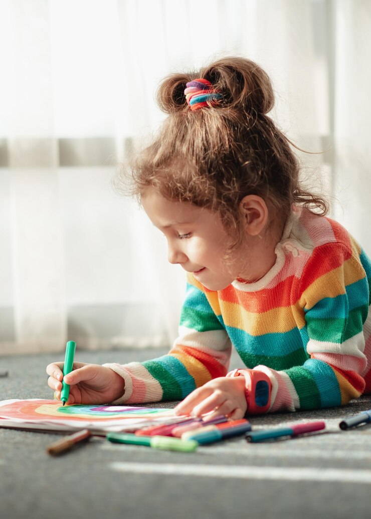 Een schattig klein meisje zit op de vloer in de stralen van de zon en tekent een regenboog met kleurrijke stift