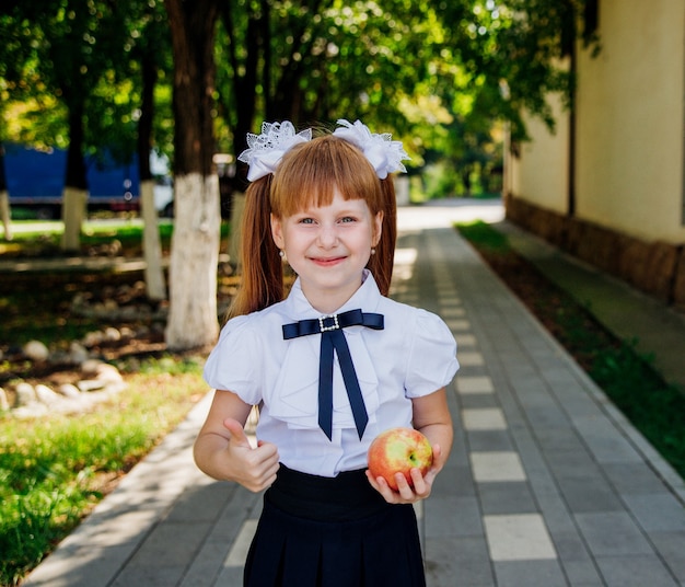 Een schattig klein schoolmeisje staat in het park of op het schoolplein en houdt een groene appel vast