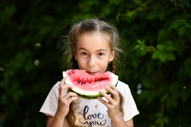 Een schattig lachend meisje eet een rode watermeloen Achtergrond van groene bladeren Nature Food Summer