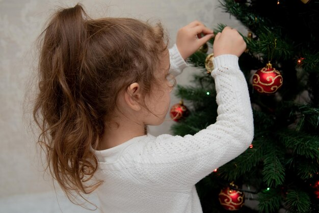 Een schattig meisje hangt speelgoed aan de kerstboom