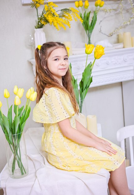 Een schattig meisje in een gele jurk met een boeket gele tulpen tegen de achtergrond gele tulpen