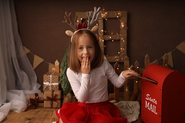 Een schattig meisje in een nieuwjaarskostuum gooit een brief aan de kerstman in de brievenbus
