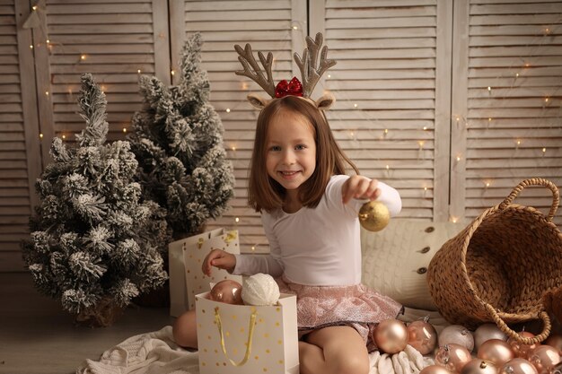 een schattig meisje in een nieuwjaarskostuum haalt een kerstbal uit een cadeauzakje