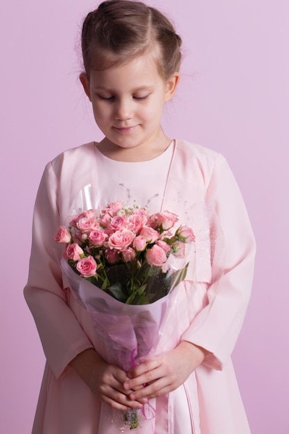 Foto een schattig meisje in een roze jurk houdt een boeket roze rozen vast.