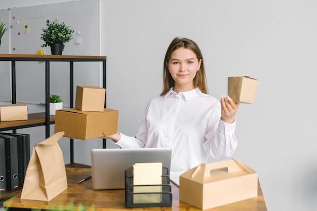 Een schattig meisje in een wit overhemd zit op kantoor met een laptop en houdt eco-voedselverpakkingen vast