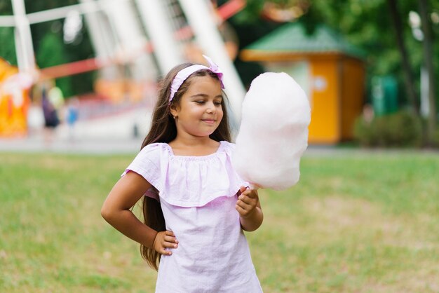 Een schattig meisje met een donkere huid in een roze jurk houdt suikerspin in haar handen in de zomer in het park