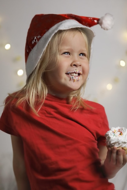 Een schattig meisje met een kerstmuts is blij en opgewonden een cake te eten