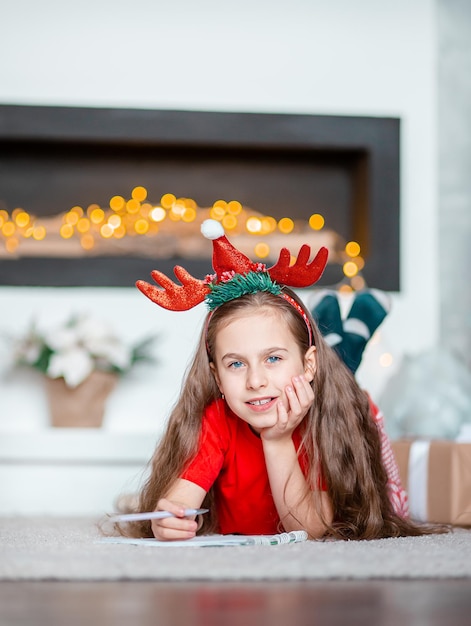 Een schattig meisje met een kerstmuts schrijft een brief aan de kerstman bij de kerstboom Gelukkige jeugd