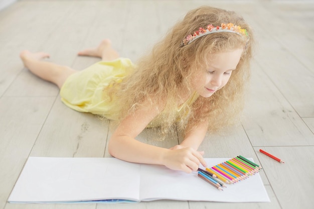 een schattig meisje met krullend haar en blauwe ogen tekent in een album met kleurpotloden