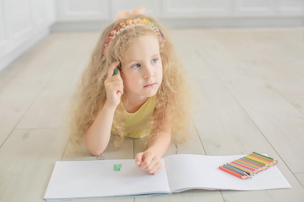 een schattig meisje met krullend haar en blauwe ogen tekent in een album met kleurpotloden