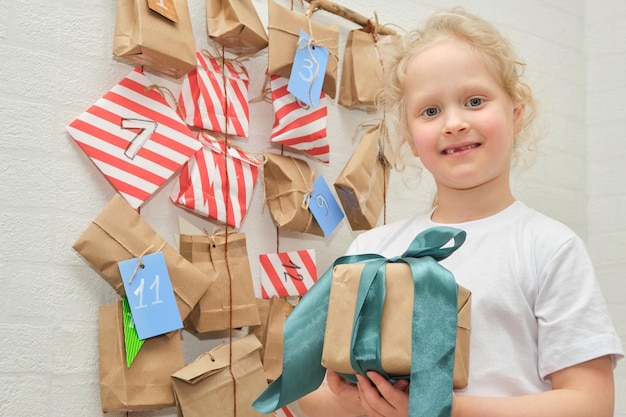 Een schattig meisje met verloren melktanden verheugt zich over een kerstcadeau tegen de achtergrond van een adventskalender