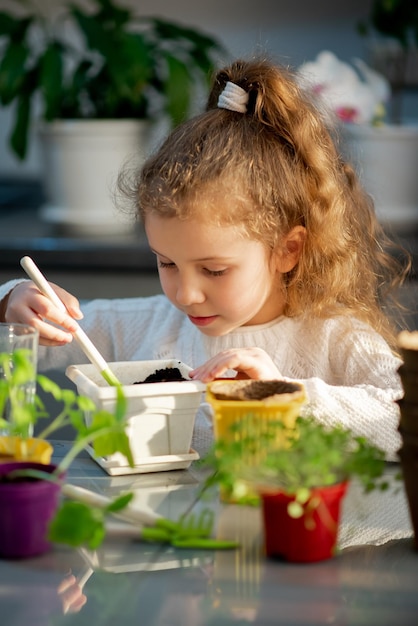 Een schattig meisje plant thuis in eco-potten Ze draagt een witte trui De tuin van het huis Hobby