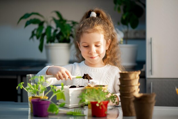 Een schattig meisje plant thuis in eco-potten Ze draagt een witte trui De tuin van het huis Hobby