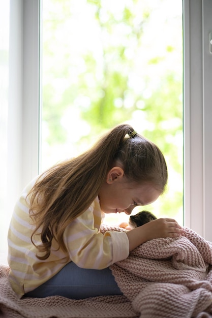 Een schattig meisje speelt met haar kleine pluizige kitten zittend op de vensterbank van het huis Vriendschap met een huisdier Lifestyle