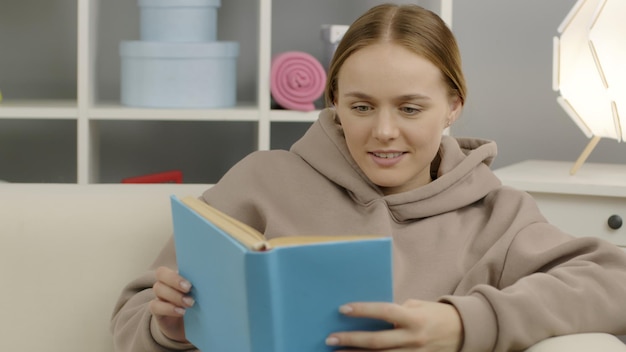 Een schattig meisje zit op de bank en leest een fascinerend boek. Onderwijs tijdens quarantaine.