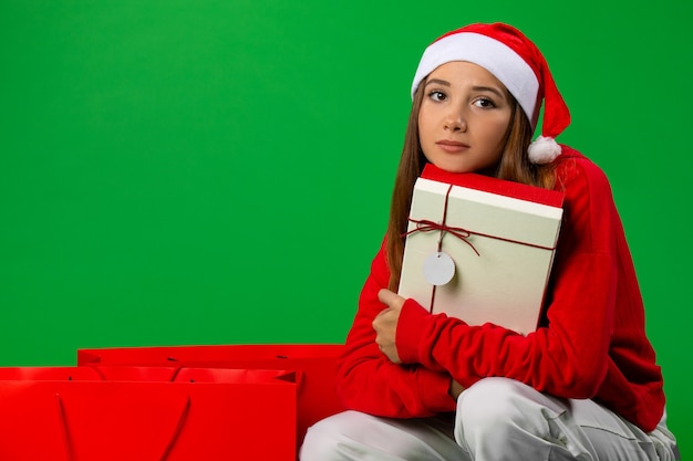 Een schattig mooi meisje met een kerstmuts omhelsde haar vakantiegift in de buurt van winterzakken en dacht na. .