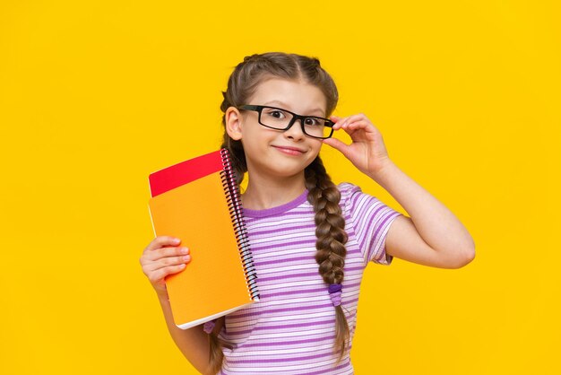 Een schattig schoolmeisje in een gestreept T-shirt houdt notitieboekjes in haar hand